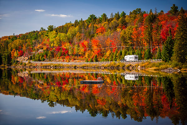 Fifth Wheel RV on the road between lake and forest during peak fall colors season.