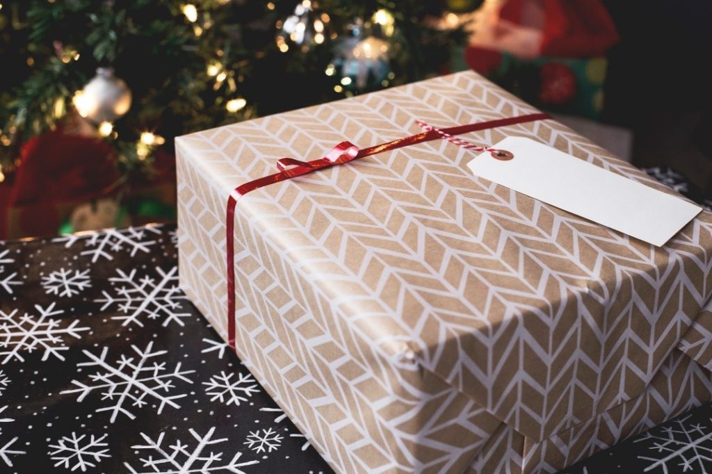 Wrapped present with a tag on table next to Christmas tree