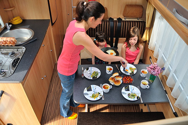 Mother setting table for family of four in RV dinette.